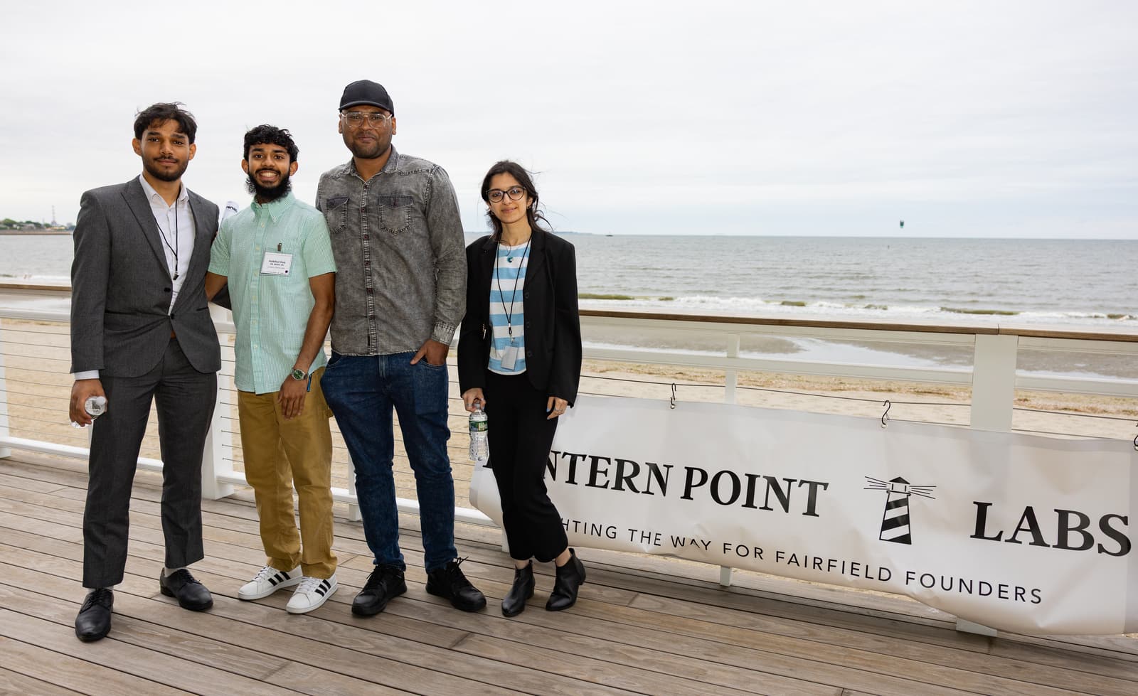 Four young professionals on the Penfield Pavilion deck beside the Lantern Point Labs banner, with the water behind them